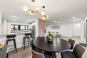 A modern kitchen with a central island, bar stools, and a dining table with a fruit bowl.