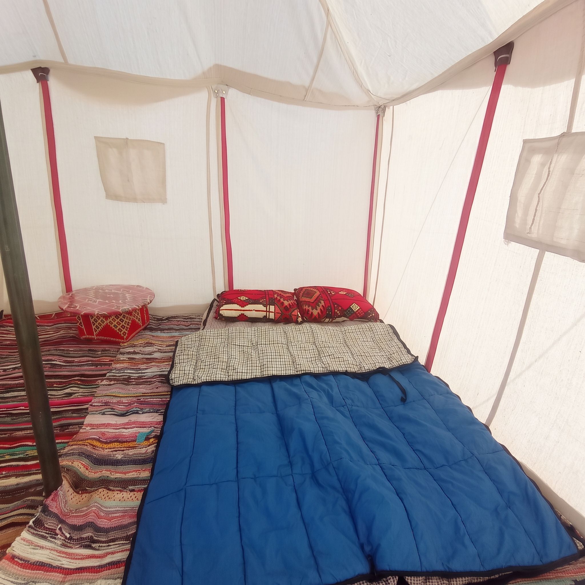 A tent with a bed, pillows, and a striped rug.