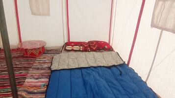 A tent with a bed, pillows, and a striped rug.