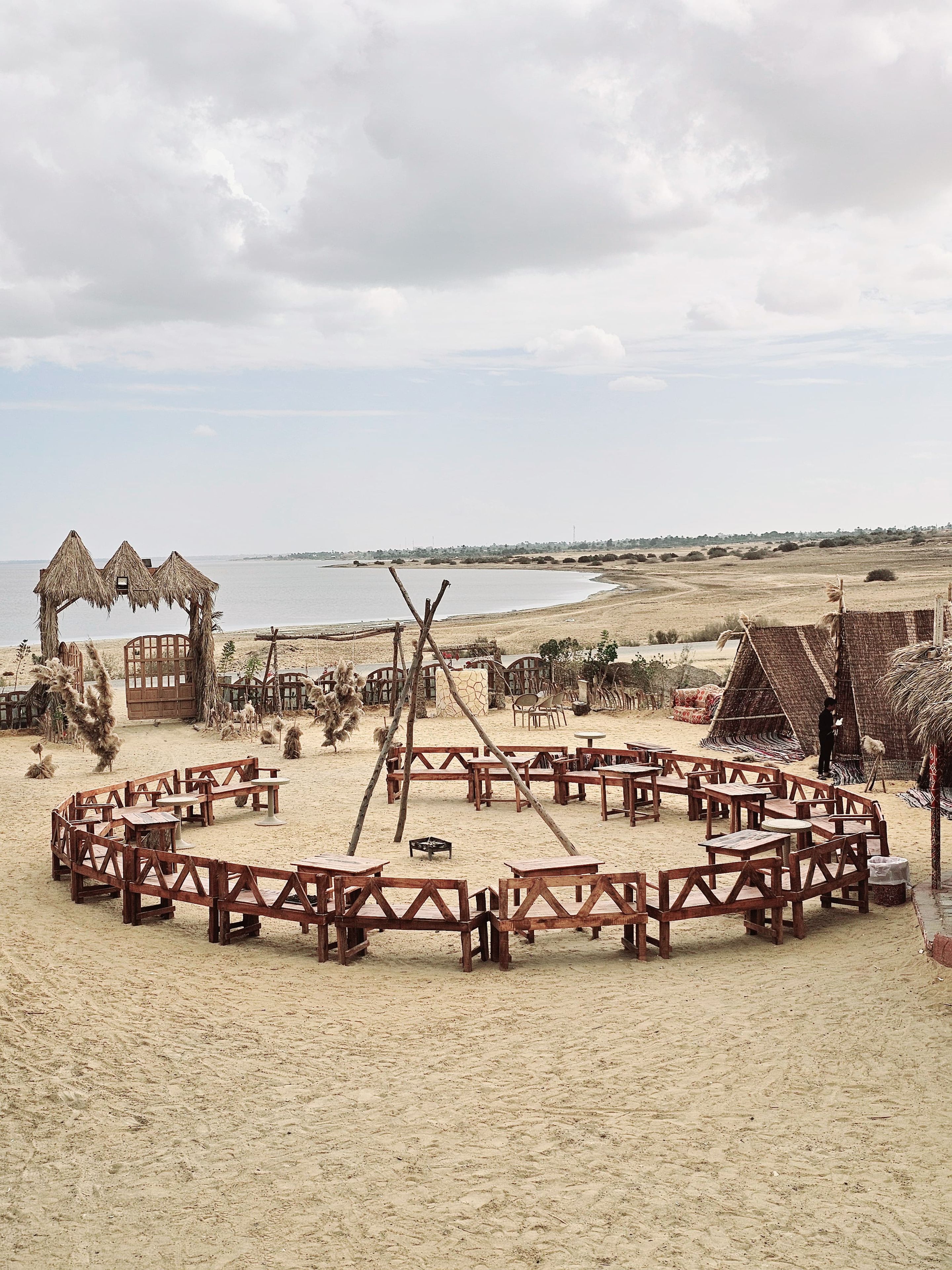 A beachside setting with wooden structures, tables, and a thatched-roof hut.