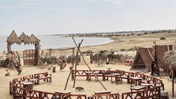 A beachside setting with wooden structures, tables, and a thatched-roof hut.