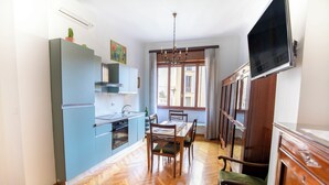Una cocina compacta con armarios azules, una mesa de comedor con sillas y un televisor colgado en la pared.