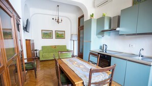 Un comedor con una mesa de madera, sillas y un sofá verde. Se observa una cocina con armarios azules y un lavamanos.