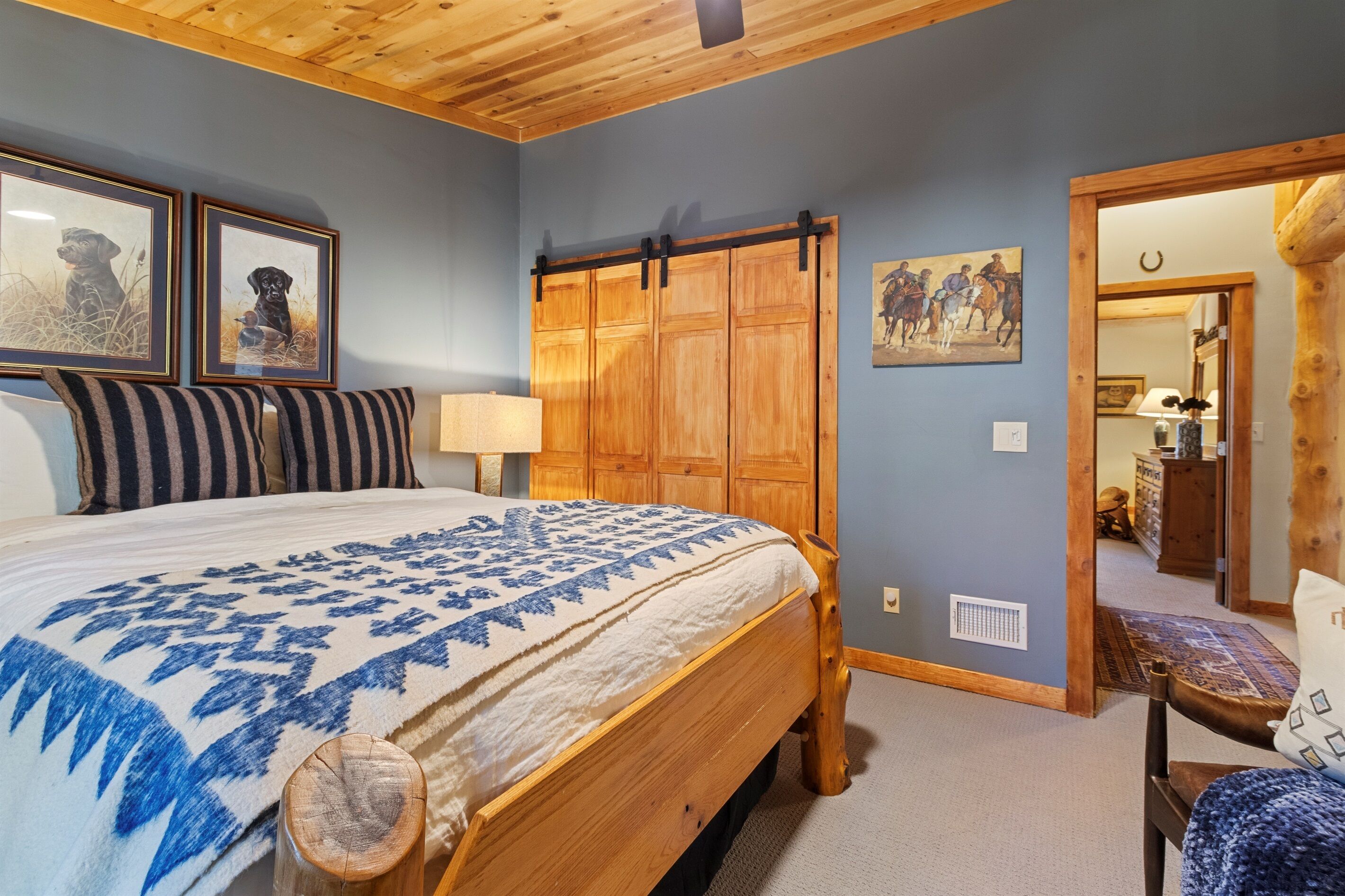 Une chambre à coucher avec un lit, une armoire en bois, des tableaux encadrés et une porte donnant sur une autre pièce.