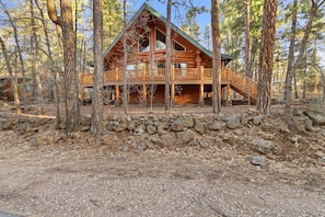 A log cabin with a porch, surrounded by trees.