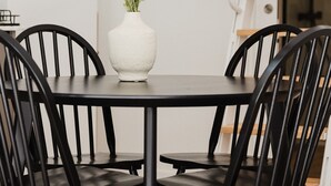 A dining table with a white vase of flowers, surrounded by black chairs.