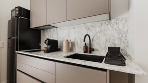 A modern kitchen with a black refrigerator, a coffee machine, a kettle, and a sink with a marble backsplash.