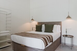 A neatly made bed with a striped blanket, a bedside table with a lamp, and a wall-mounted shelf.