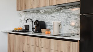 Een moderne keuken met houten kastjes, een marmeren aanrecht, een koffiezetapparaat, een waterkoker, en een mand met sinaasappels.