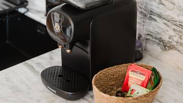 Une machine à café est posée sur un plan de travail en marbre, à côté d’un panier contenant des sachets de thé Twinings.