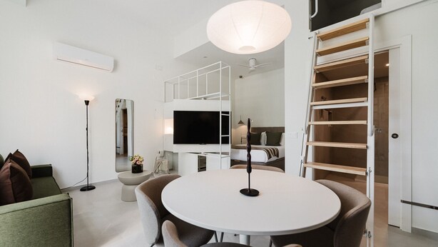 Een moderne, goed verlichte kamer met een ronde tafel, stoelen, een grote spiegel en een televisie.