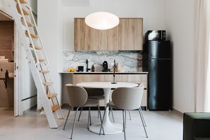 A modern kitchen with a white dining table, four chairs, a black refrigerator, wooden cabinets, and a marble backsplash.