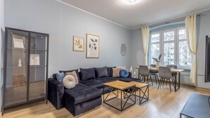 A modern living room with a dark sofa, a wooden coffee table, and a dining area with chairs and a table. - Apartamenty Sun & Snow Szczytnicka (Wroclaw)