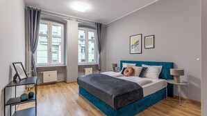 A bedroom with a bed, two bedside lamps, a radiator, a shelf with decorative items, and two windows with curtains. - Apartamenty Sun & Snow Szczytnicka (Wroclaw)