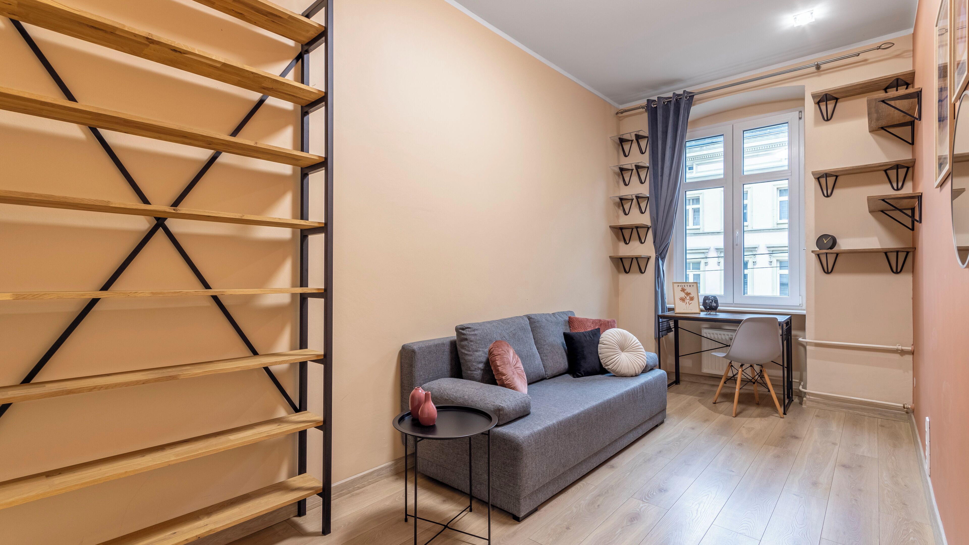 Ein modernes Wohnzimmer mit einem grauen Sofa, einem kleinen runden Tisch und einem Fenster mit Vorhängen.