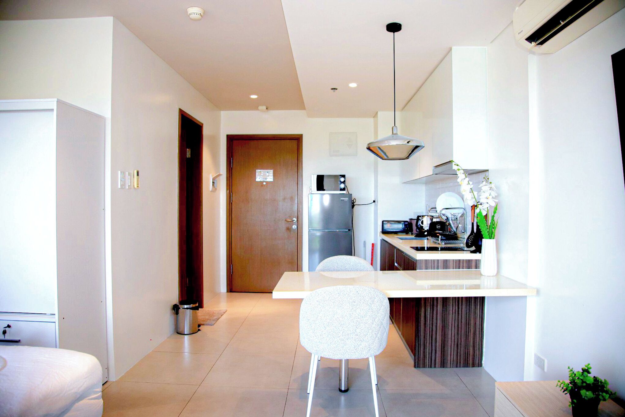 A modern kitchen with a refrigerator, microwave, and sink. There is a dining area with a white chair and a small table.