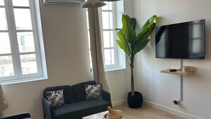A modern living room with a sofa, a coffee table, a TV mounted on the wall, and a potted plant.