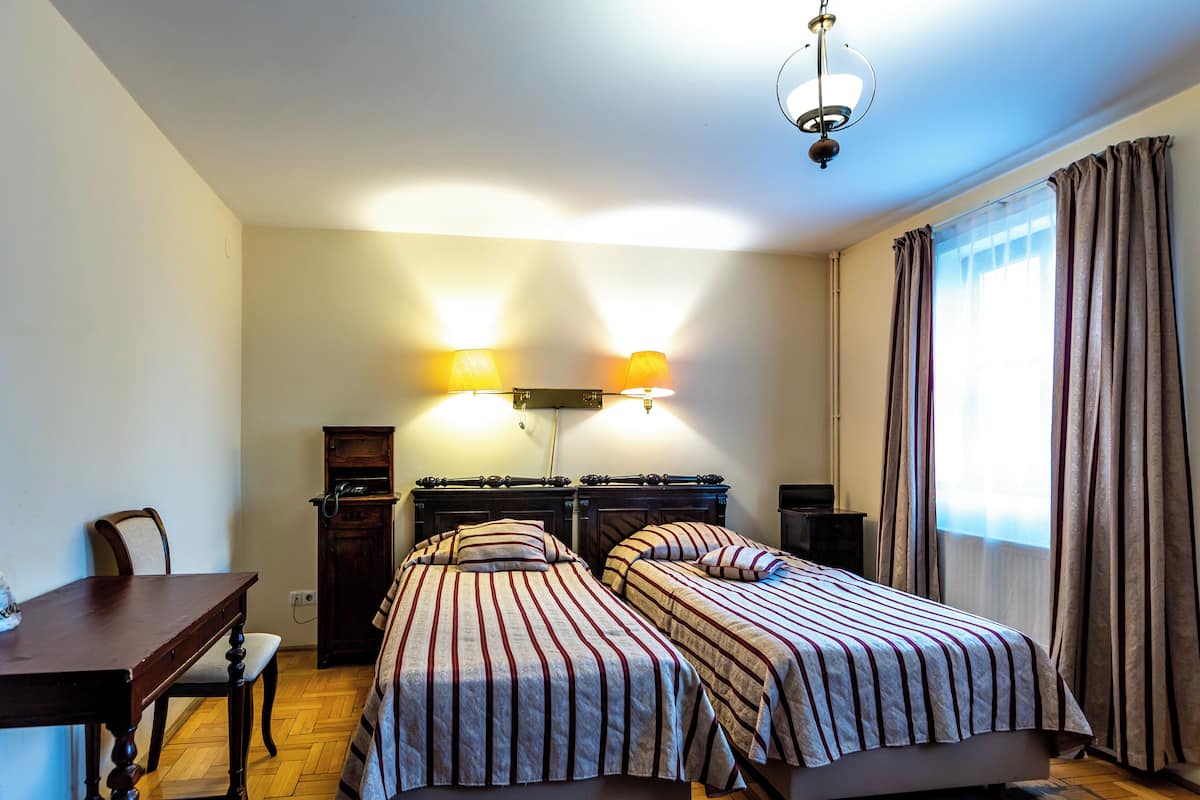 Une chambre avec deux lits, un bureau et une chaise. Il y a deux lampes fixées au mur et un luminaire au plafond.