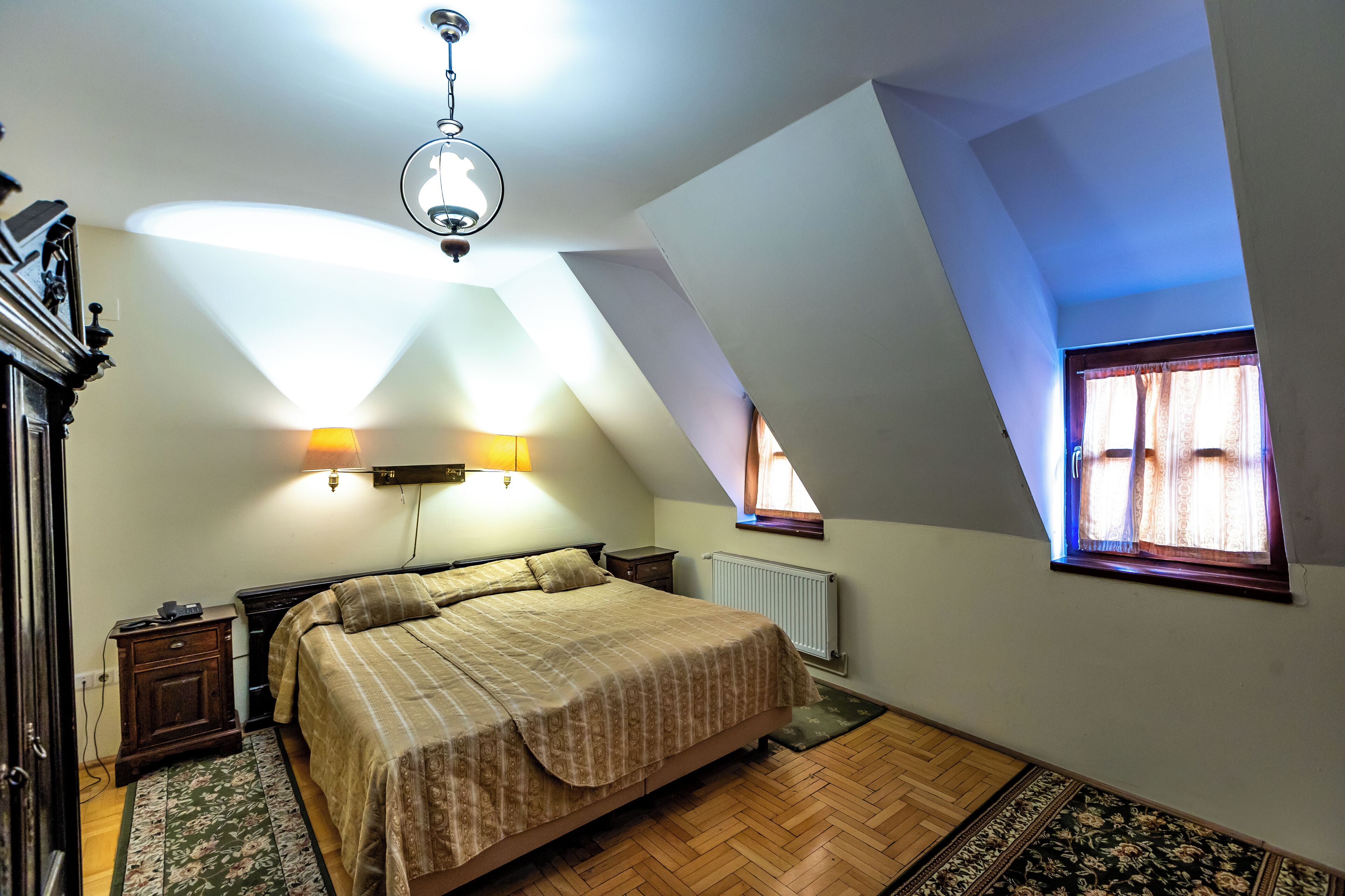 Ein Schlafzimmer mit einem großen Bett, Holzboden, einem Heizkörper und einem Fenster mit Vorhängen.