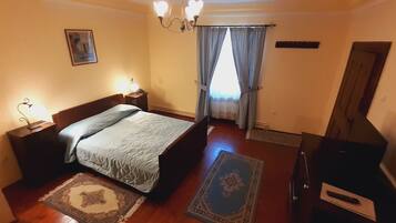 A bedroom with a bed, nightstands, a dresser, a chandelier, and a window with curtains.
