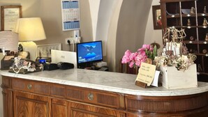 Un área de recepción con mostrador de mármol, armarios de madera, una lámpara de araña, un reloj, una radio y un monitor de computadora.