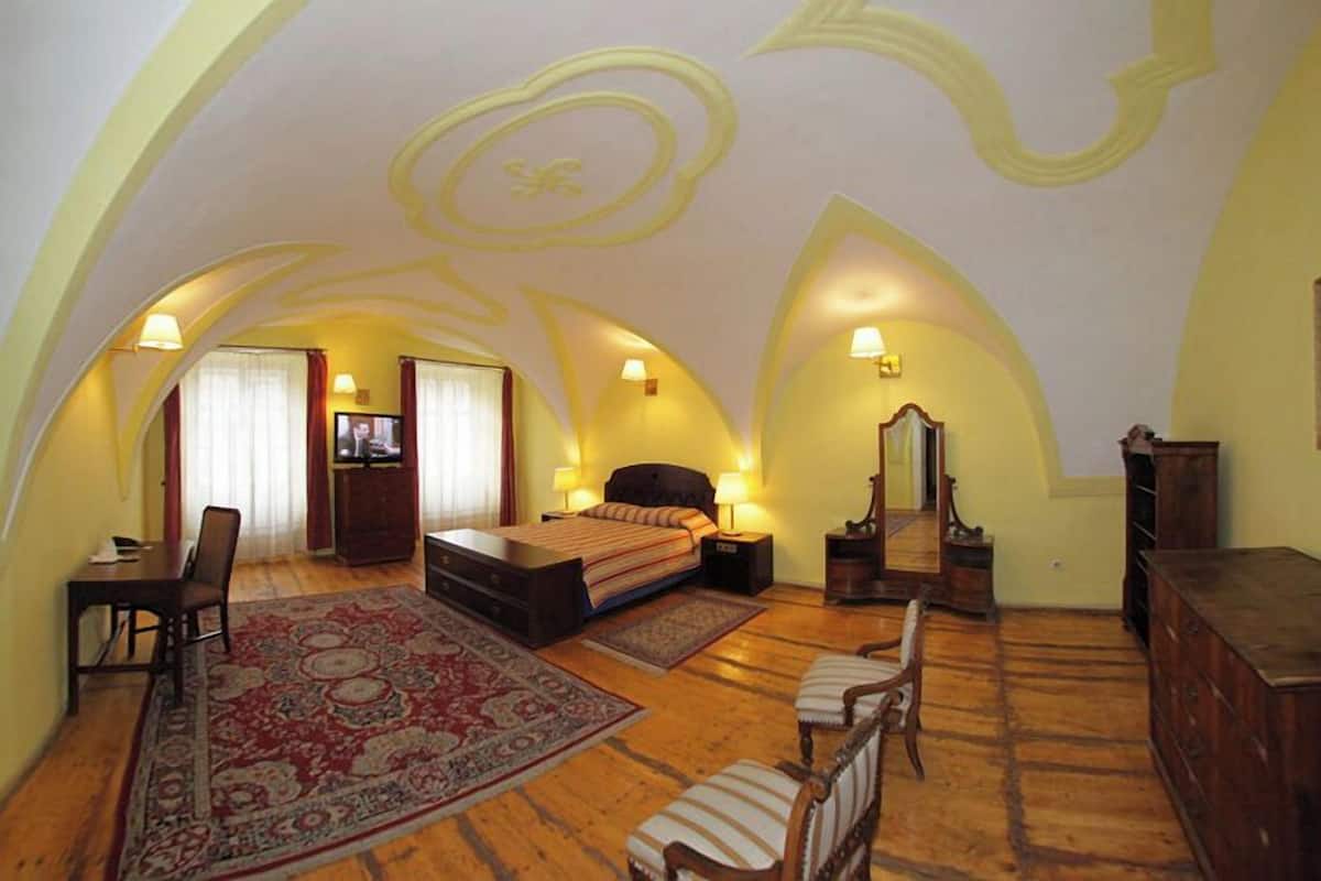Une chambre avec un grand lit, un bureau, une chaise, une commode et un miroir. La pièce est dotée d’un plancher en bois et d’un tapis à motifs.