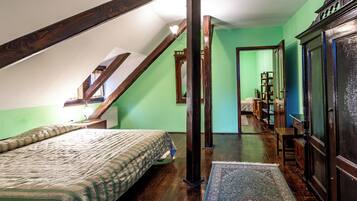 A bedroom with a sloped ceiling, a bed with a patterned bedspread, a wooden wardrobe, and a mirror.