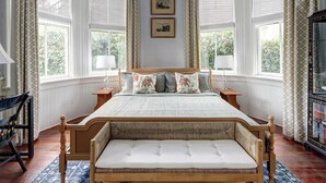 A bedroom with a large bed, two bedside tables, a bench at the foot of the bed, and a large window with curtains.