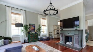 A living room with a fireplace, a flat-screen TV, a sofa, a coffee table, and a lamp. - The Koi Escape, Victorian | Upper Porch | Parking (Savannah)