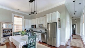 A kitchen with white cabinets, a stainless steel refrigerator, a dining table with chairs, and hanging pendant lights. - The Koi Escape, Victorian | Upper Porch | Parking (Savannah)