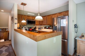 A kitchen with wooden cabinets, a stainless steel refrigerator, a built-in oven, and pendant lighting.