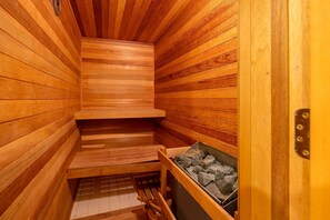 Una sauna con paredes y bancos de madera, una puerta de metal y un recipiente lleno de piedras.