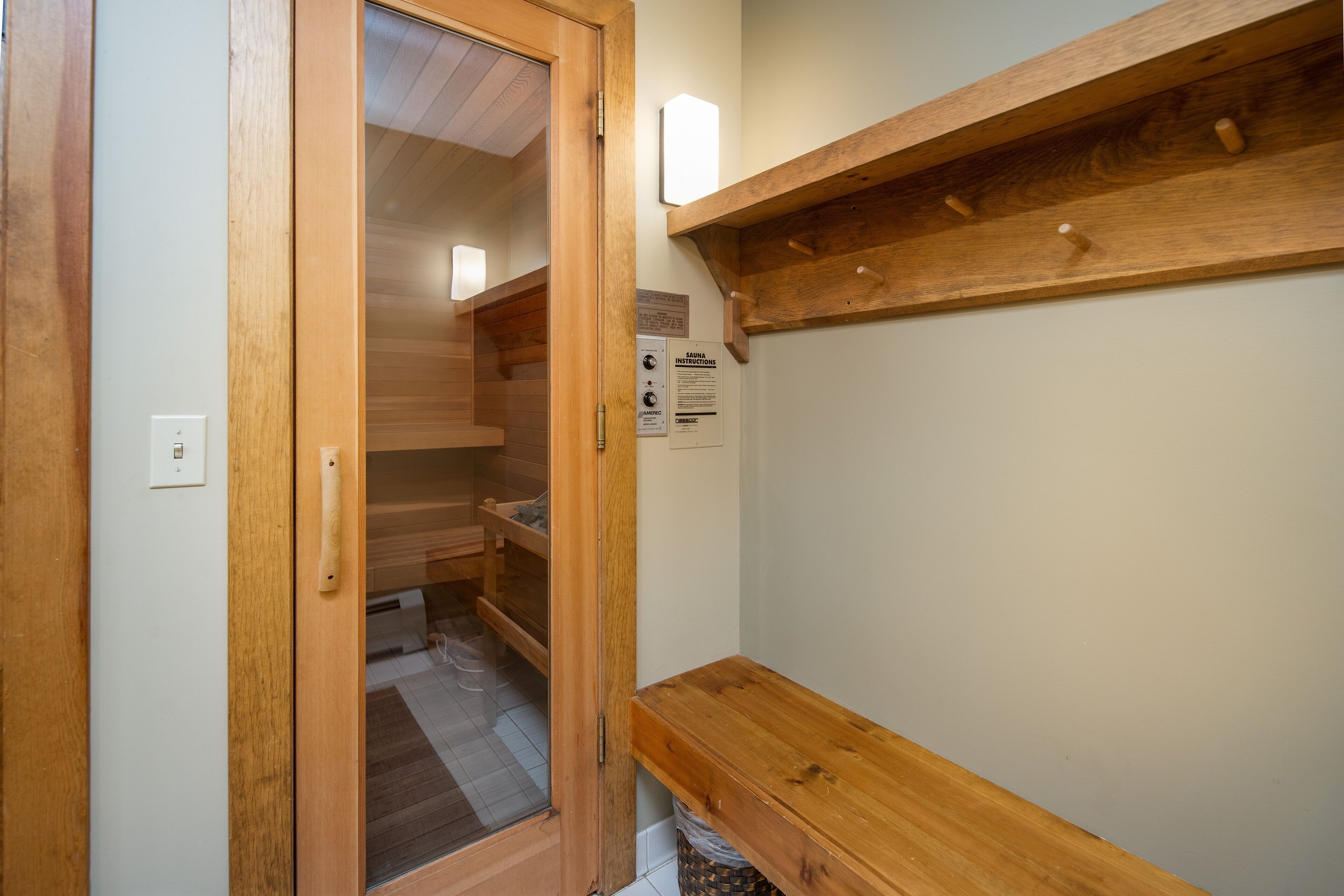 Un interior de madera con un banco, un estante de madera y una puerta que da a una habitación con piso de baldosas.