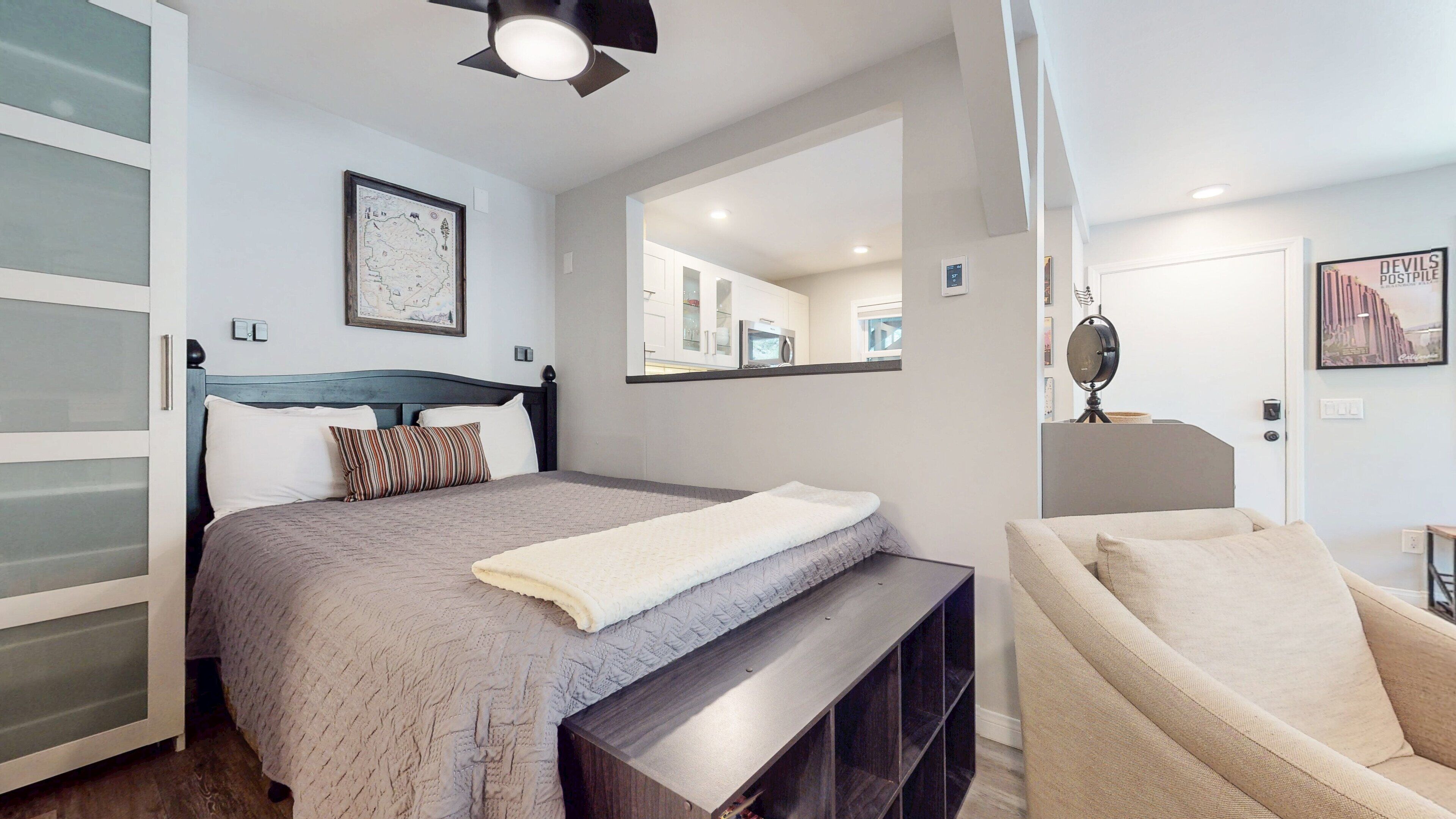 A bedroom with a bed, a bedside table, a chair, a wardrobe, a mirror, and a map on the wall.