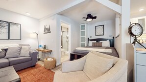 Una sala de estar moderna y luminosa con un sofá gris, un sillón beige y una mesa de centro de madera. Hay una alfombra pequeña en el suelo, una cesta con objetos y un mapa enmarcado en la pared.