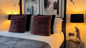 A neatly made bed with two large pillows, a bedside lamp, and abstract art on the wall. - Historic 5* Tudor Residence: Penthouse (Manchester)