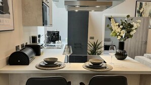 A modern kitchen with a central island, black chairs, a coffee machine, and a vase with flowers. - Historic 5* Tudor Residence: Penthouse (Manchester)