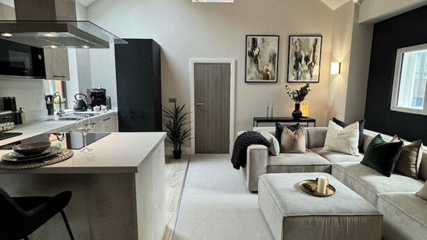 A modern kitchen with a central island, a dining area with a sofa and table, and a living room with a large window. - Historic 5* Tudor Residence: Penthouse (Manchester)