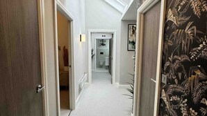 A narrow hallway with a carpeted floor, leading to a bathroom with a glass door. - Historic 5* Tudor Residence: Penthouse (Manchester)