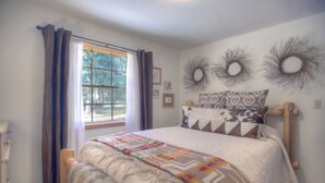 Een slaapkamer met een groot raam, een bed met beddengoed met een patroon, en decoraties aan de muur.