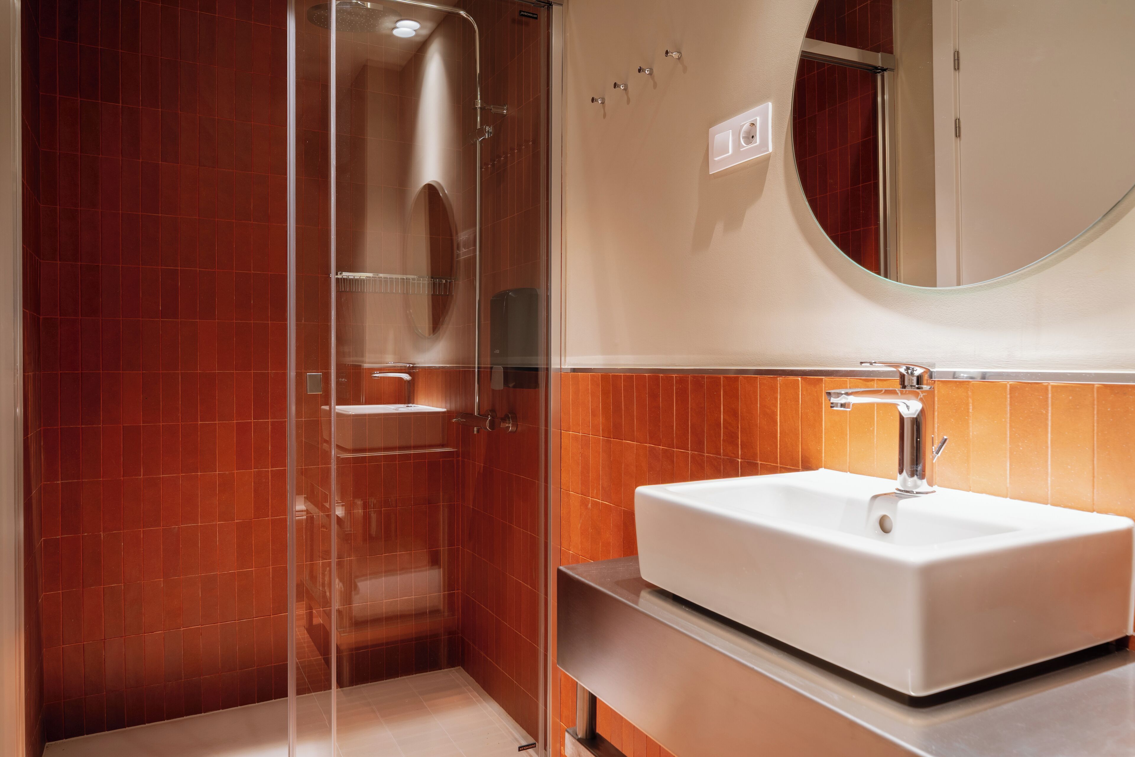 Un baño moderno con ducha envuelta en vidrio, un lavabo blanco y un espejo encima.