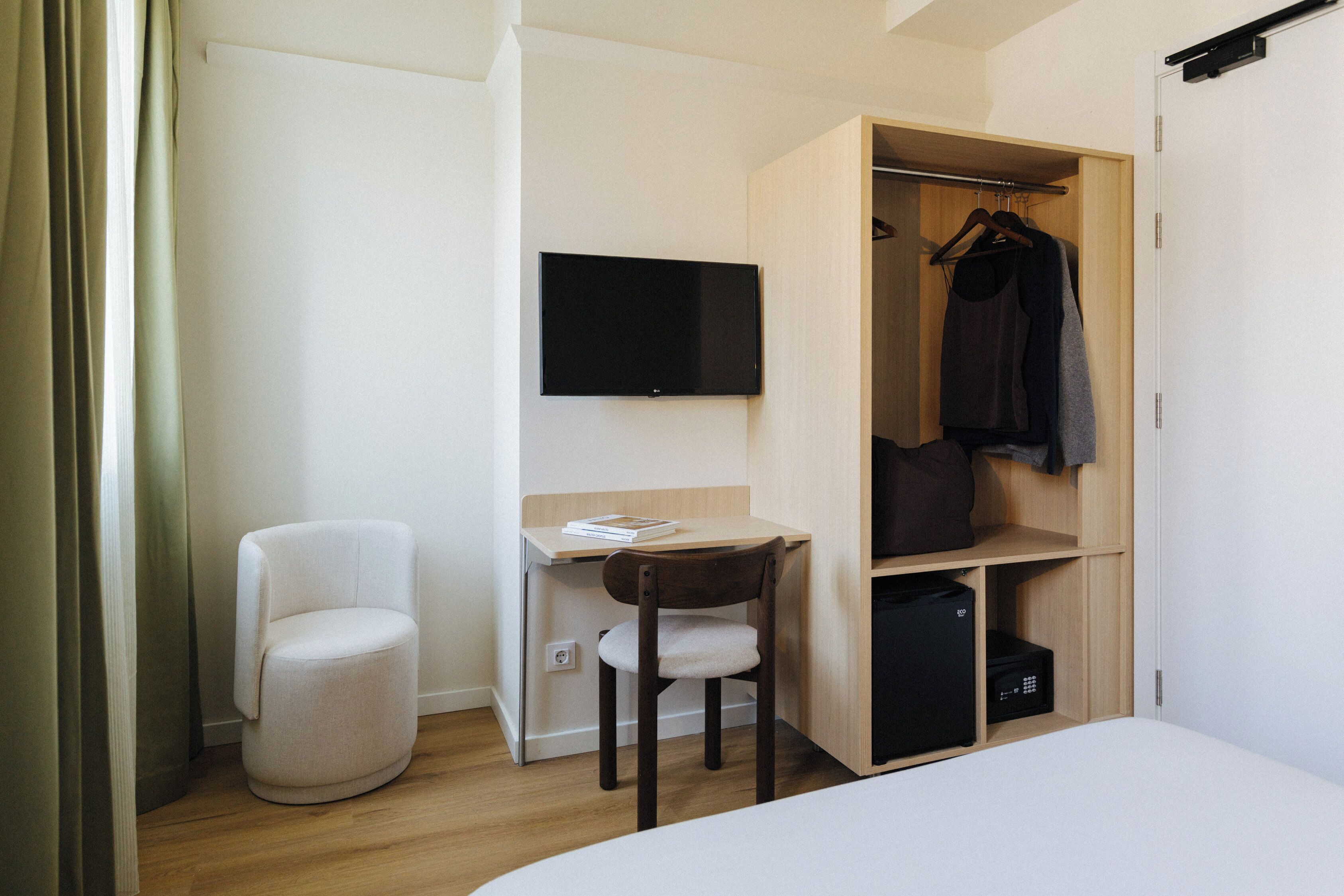 Ein kleines Hotelzimmer mit einem Bett, einem Schreibtisch mit Stuhl, einem Fernseher und einem Kleiderschrank.