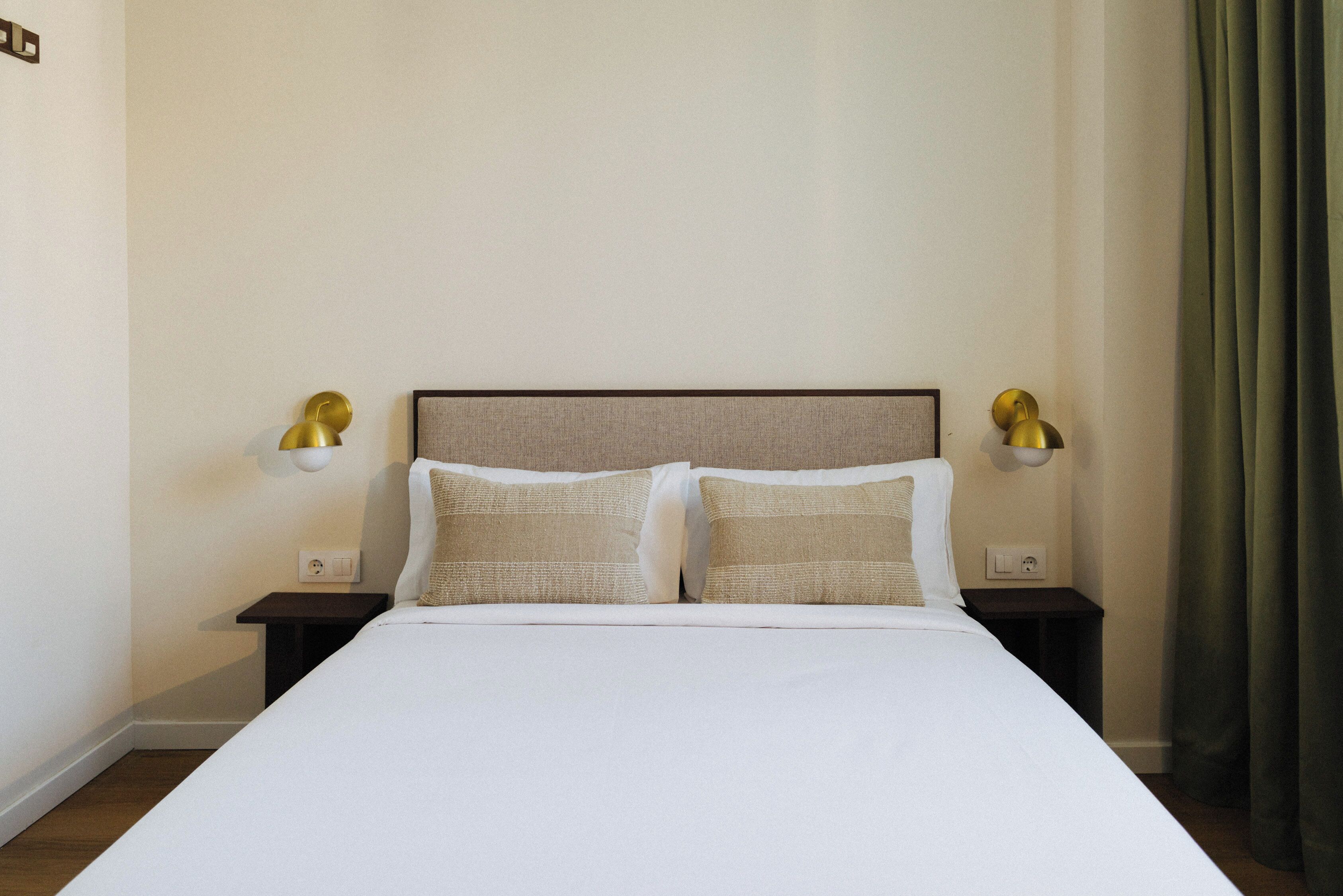 Una cama bien hecha con sábanas blancas y dos almohadas, flanqueada por dos mesitas de noche con lámparas.