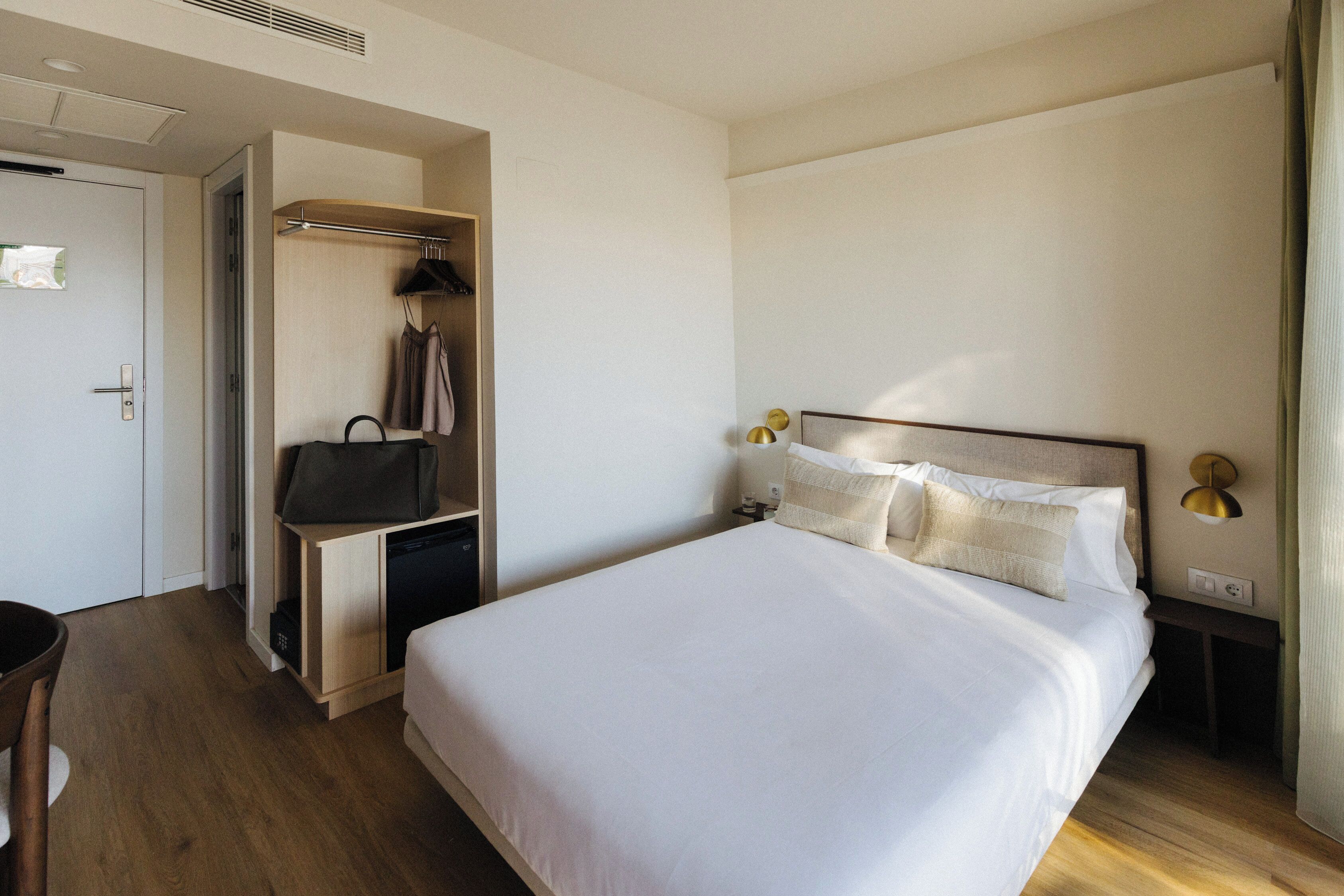 Una habitación de hotel con cama, mesitas de noche, armario y escritorio con silla.