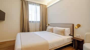 Habitación de hotel ordenada con una cama grande, una mesita de noche, una silla y un televisor montado en la pared.