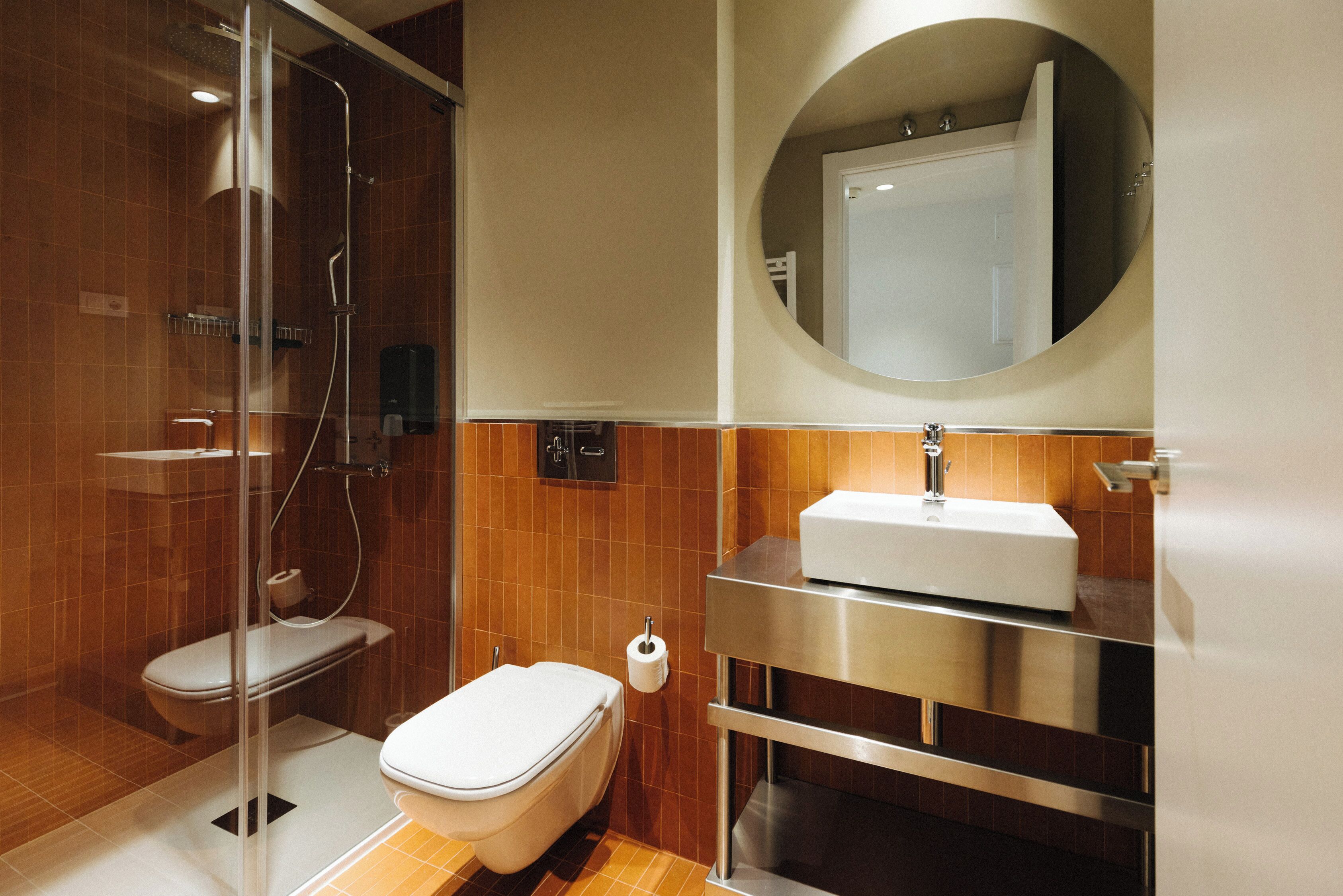Un baño moderno con ducha envuelta en vidrio, inodoro blanco, lavamanos con espejo y un perchero para toallas.