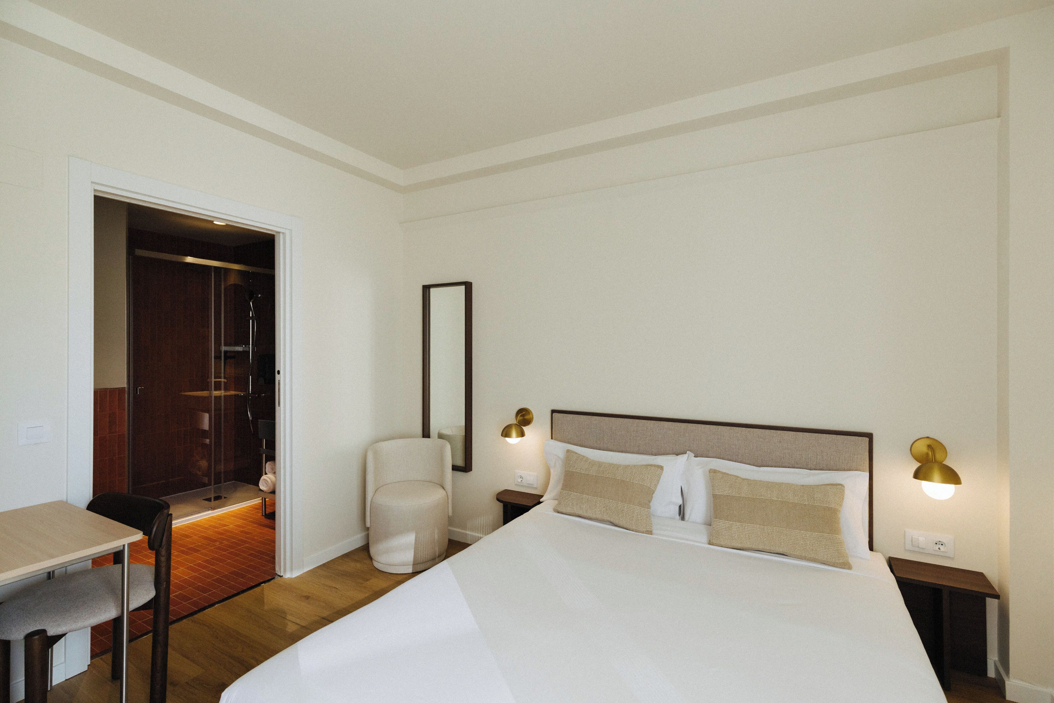 A hotel room with a bed, a chair, a desk, and a mirror.