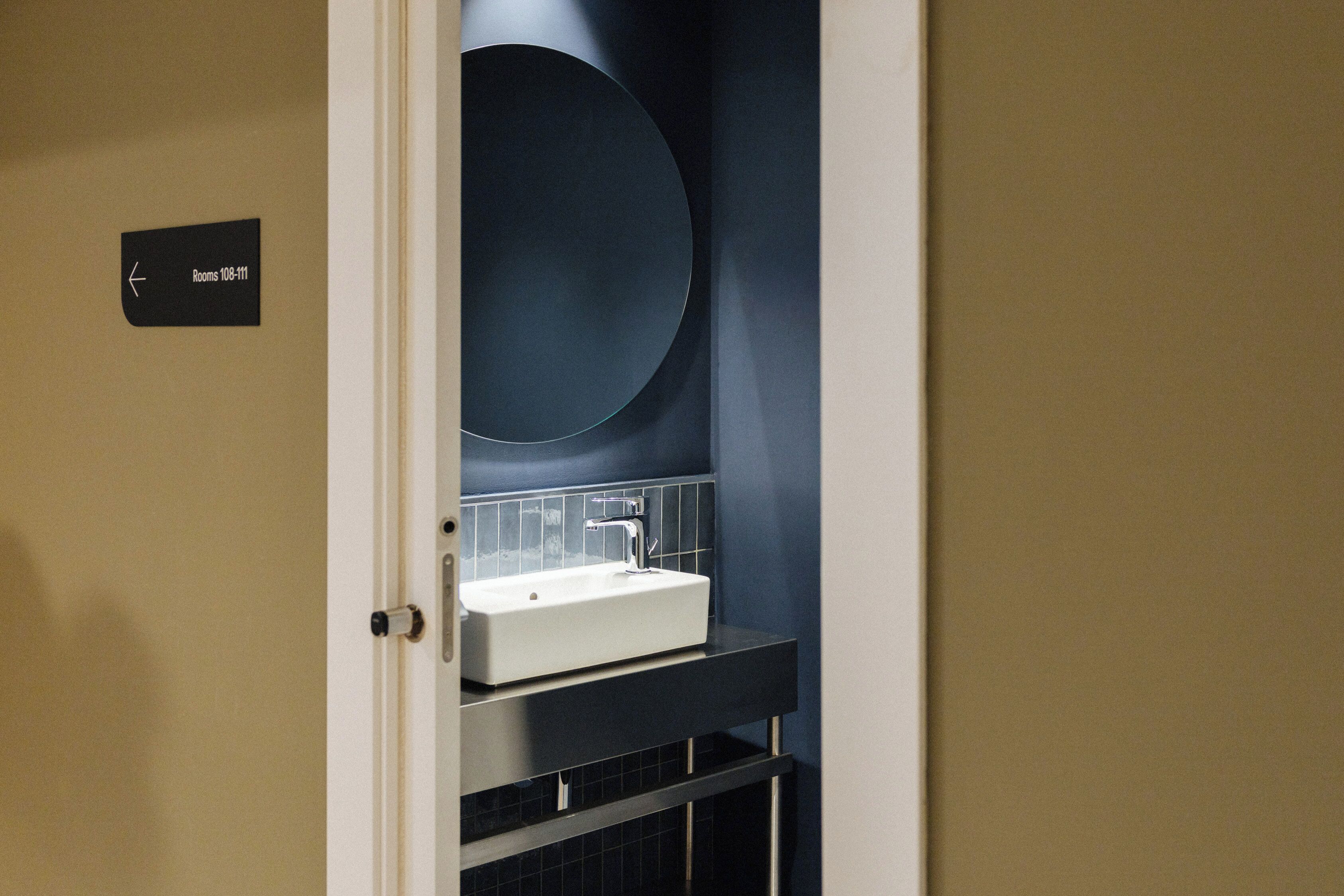 A bathroom with a white sink, dark blue walls, and a large mirror.