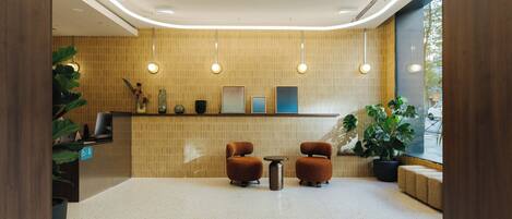 Un hall con mostrador de recepción, dos sillones, una mesita y una planta en maceta.