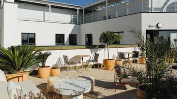 Un patio al aire libre moderno con mobiliario, plantas en macetas y una vista despejada de la arquitectura del edificio.